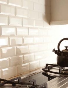 Kitchen backsplash uses cream beveled subway tiles for a sophisticated look