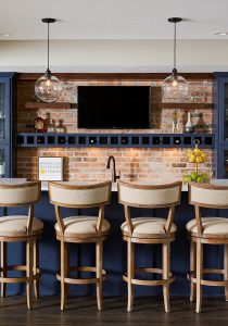 A basement bar gets an infusion of personality with a pop of blue similar to Classic Blue; paired with an exposed brick wall, it feels both modern and traditional at once. / Design by Sneak Peek Design