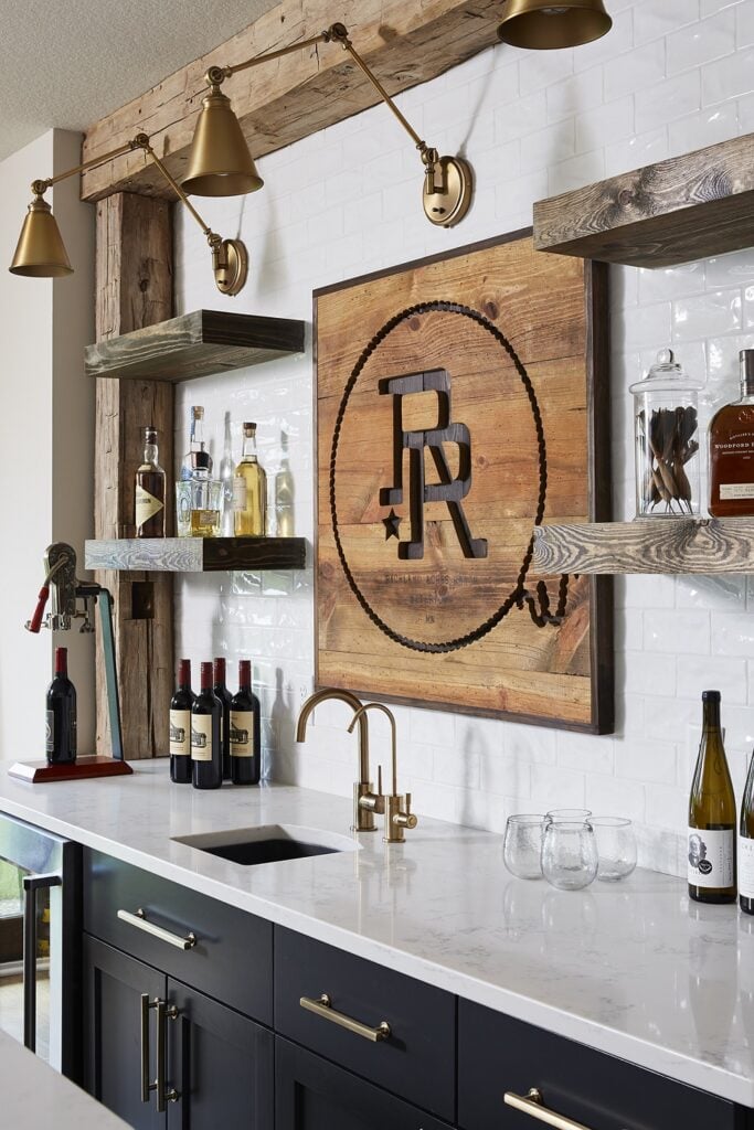 Basement bar with white tile backsplash with  Sherwin Williams Iron Ore cabinets and gold hardware and wall sconce lighting